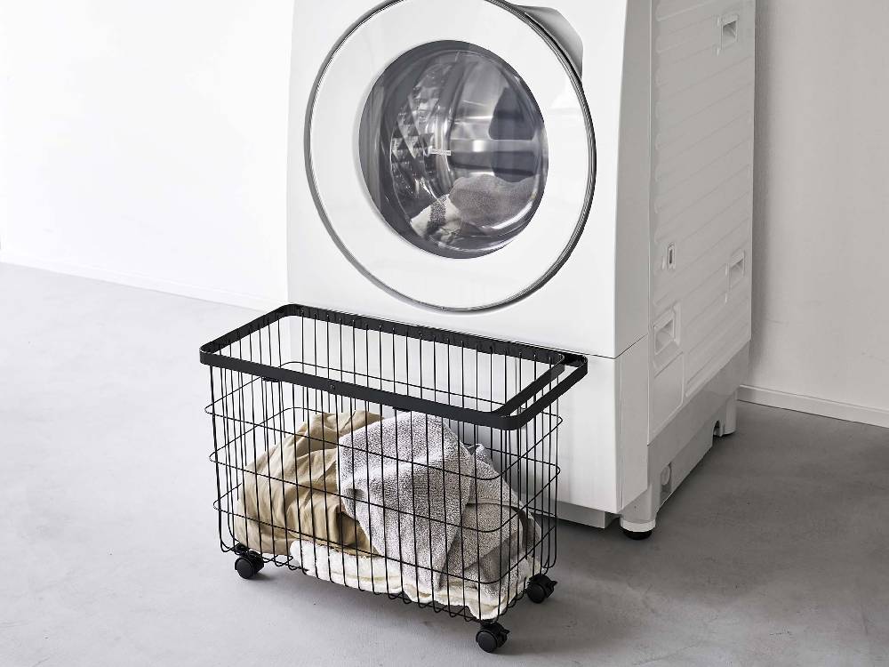 キャスター付きワイドランドリーバスケットが洗濯機と衣類乾燥機のあるランドリールームに配置されている様子