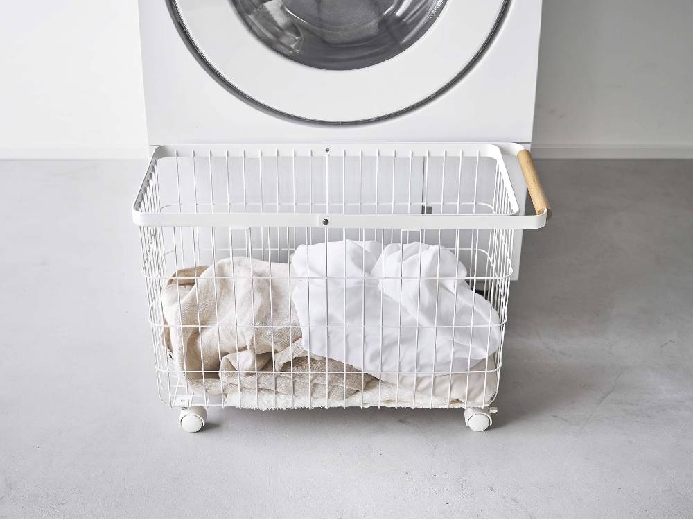 キャスター付きワイド＆ローのトスカランドリーバスケットが洗濯機と衣類乾燥機の隣に置かれた洗濯室の様子