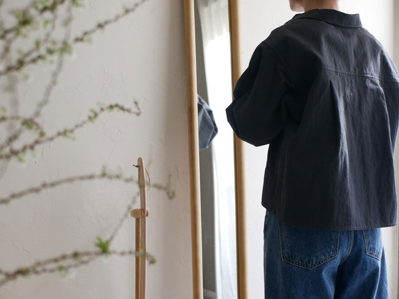 サンフラワーラタン製のHOKOS全身映るチークスリムミラーに、デニムの袖や襟、ポケットを持つ人の背中が映っています。