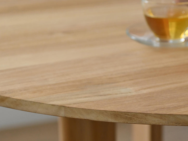 サンフラワーラタンのHOKOS製チークラウンドダイニングテーブル。木製の屋外用コーヒーテーブルの上に花束が飾られている