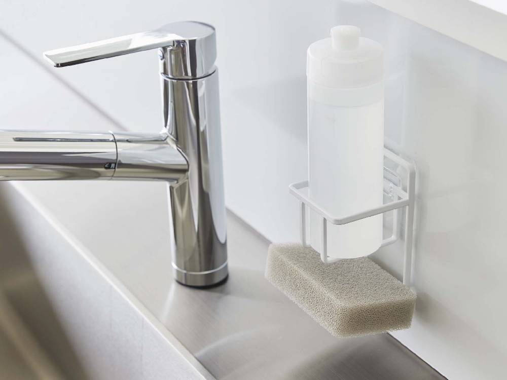 キッチンの光沢ある壁面に取り付けられたタワー型フィルムフックスポンジ＆ボトルホルダーと、周囲に配置されたボトルや花鉢の様子