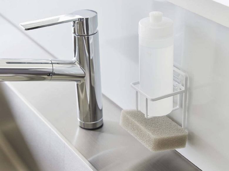 キッチンの光沢ある壁面に取り付けられたタワー型フィルムフックスポンジ＆ボトルホルダーと、周囲に配置されたボトルや花鉢の様子