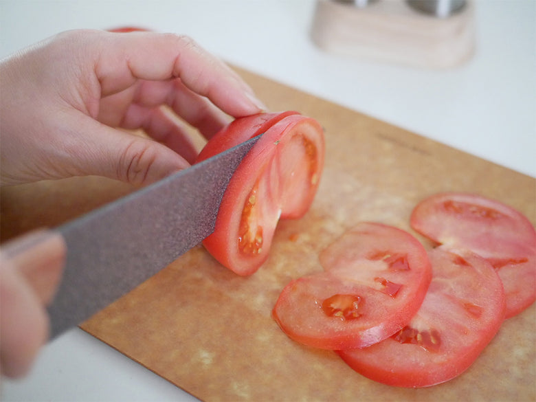 協和工業のスーパーストーンバリア包丁と専用シャープナーが調理台に配置され、新鮮なトマトや野菜を切るために使用されているキッチンシーン