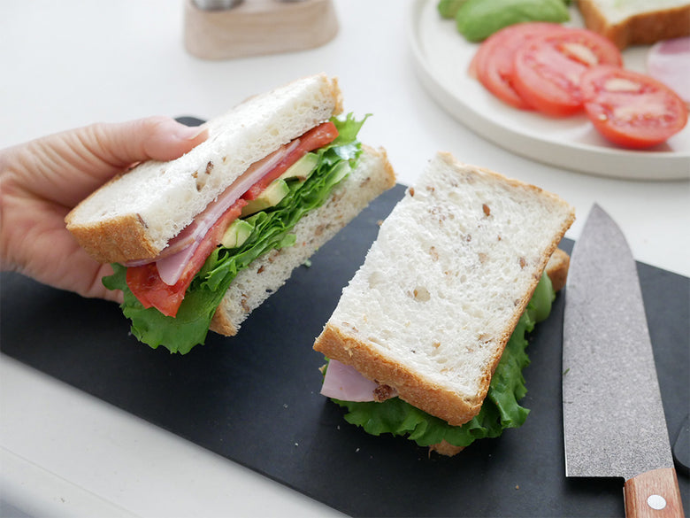 キッチンテーブルに協和工業のスーパーストーンバリア包丁と専用シャープナーが配置され、新鮮な野菜やサンドイッチなど多彩な食材が並んでいる様子