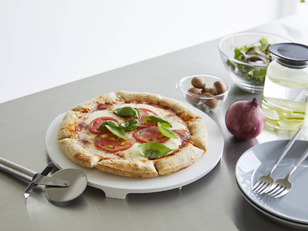 マグネット付き抗菌まな板がテーブルウェアやピザ、チーズなどの食材と共にキッチンに配置されている様子