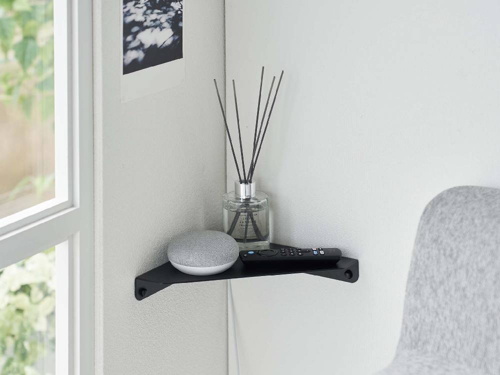 石こうボード壁に取り付けられた灰色の「tower」コーナーシェルフ。上にはランプや絵画、ガジェットが配置されています