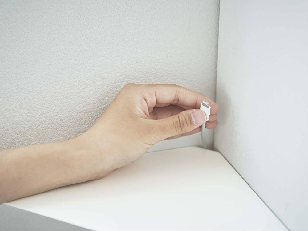 白色のタワー型コーナーシェルフが石こうボードの壁に取り付けられており、近くにライトスイッチが見える様子