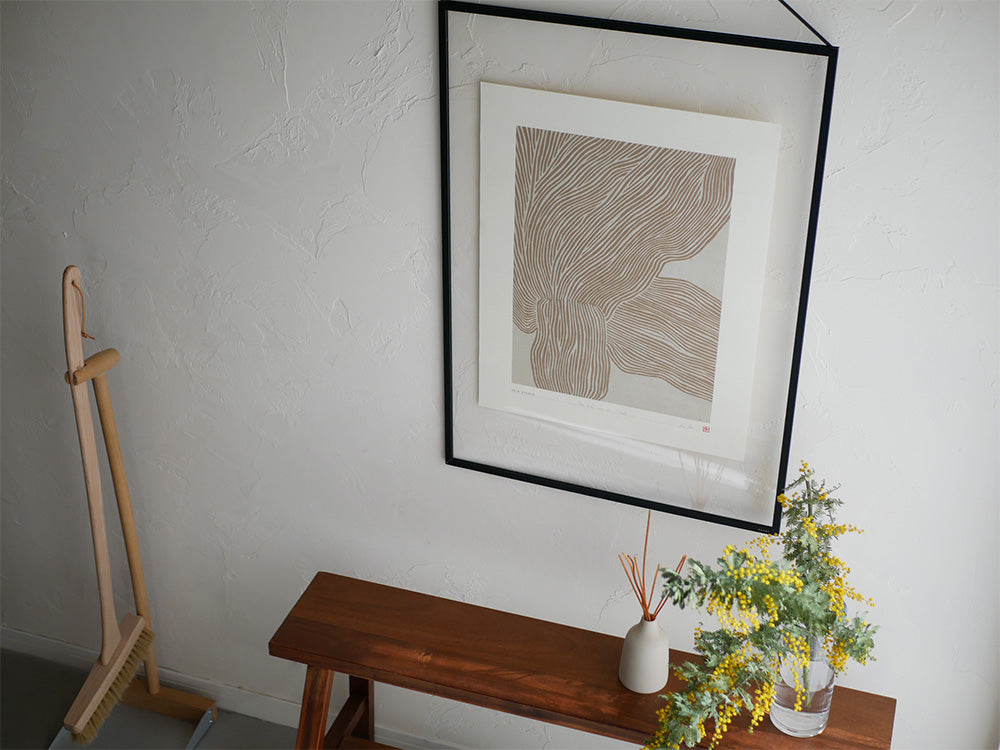 HEIN STUDIOのアートポスターが木製フレームに入れられ、木の床や花鉢と共にスタイリッシュな室内に飾られています。