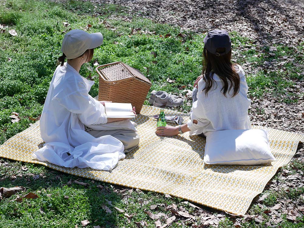 シセイの洗えるレジャーマットの上で帽子を被った人々がピクニックを楽しみながらバスケットと共にくつろいでいる様子