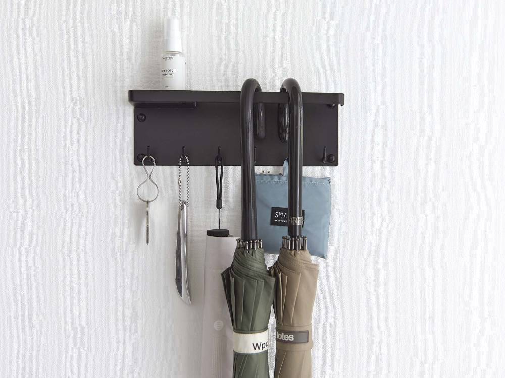 石こうボードに取り付けられたスチール製トレー付きアンブレラホルダーで、衣類掛けやキッチン用品が整理されています