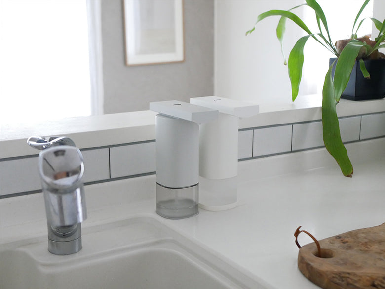 シルバー色のオートディスペンサーがキッチンのカウンタートップに設置されており、近くにシンクや蛇口が見える様子