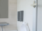 グレー色のマグネット式ソープディスペンサーとトイレットペーパーホルダーが設置されたモダンなバスルームの設備