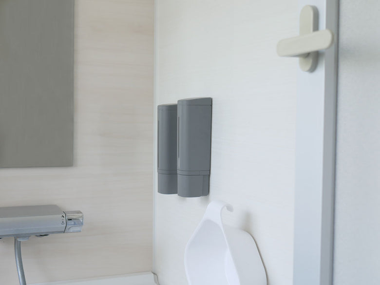 グレー色のマグネット式ソープディスペンサーとトイレットペーパーホルダーが設置されたモダンなバスルームの設備