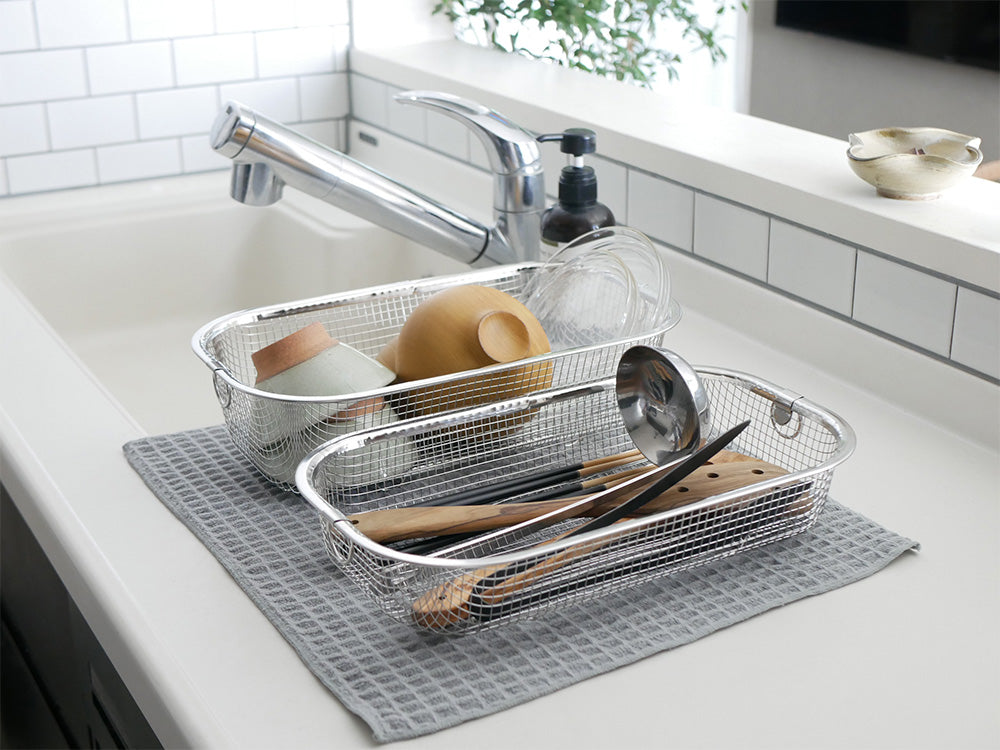 キッチンシンクに置かれたステンレス製のすっきり暮らす水切りかご。テーブルウェアや調理器具が整然と収納されています。