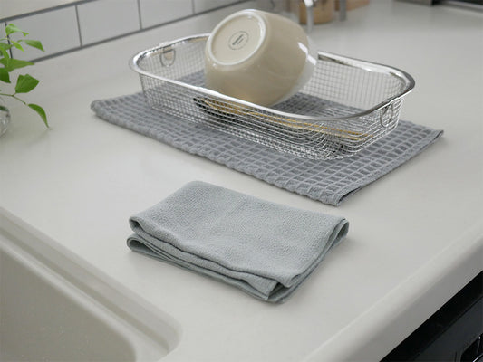 テイジンのあっちこっちふきんMサイズと厚手サイズのグレーおよびホワイト色のキッチン用ふきんが食器やキッチン用品と共にキッチンのシンク周りに配置されている様子