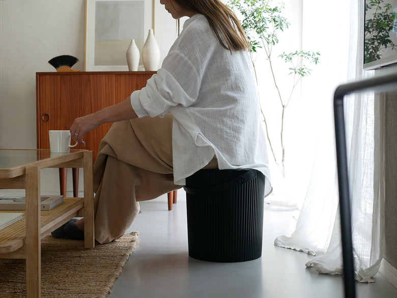 リビングルームの木製フロアに置かれた【八幡化成】オムニウッティ ニュートラルの蓋付き収納スツール