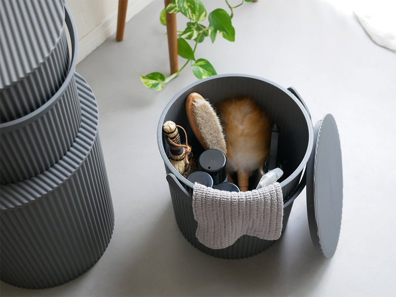 灰色のプラスチック製蓋付きシリンダー型収納バスケットで、メッシュとシルバーのディテールが特徴的。スツールとしても使用可能なデザイン。