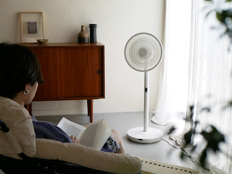 リビングルームに設置されたシロカの人認識センサー付きDC扇風機と木製フローリング、観葉植物、ランプが配置されたインテリア