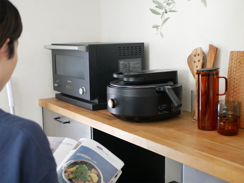 AINXの全自動調理スマートオートクッカーと付属の鍋や蓋がキッチンに配置されている様子