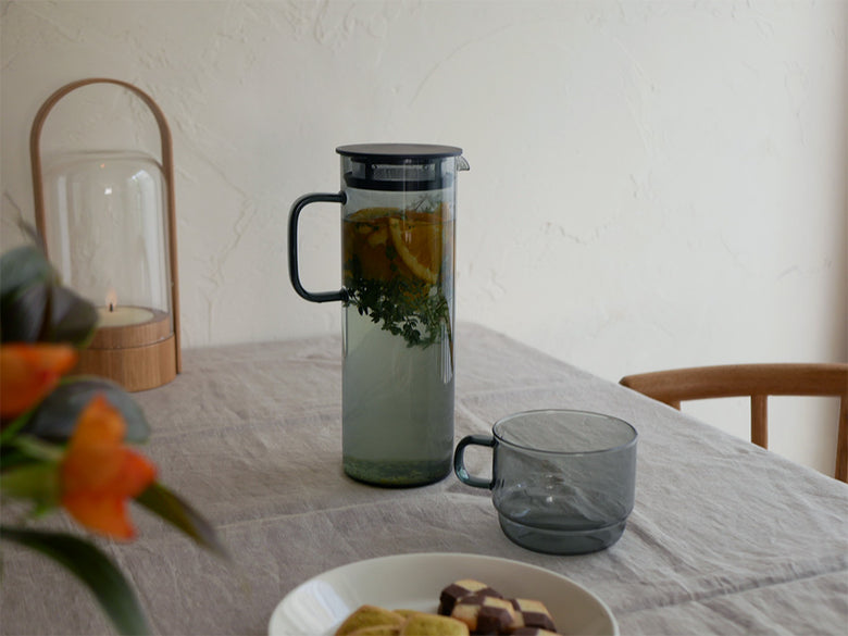 HARIOのグレーとアンバー色の耐熱ガラスコールドブリューピッチャーとスタックマグカップが並べられた画像