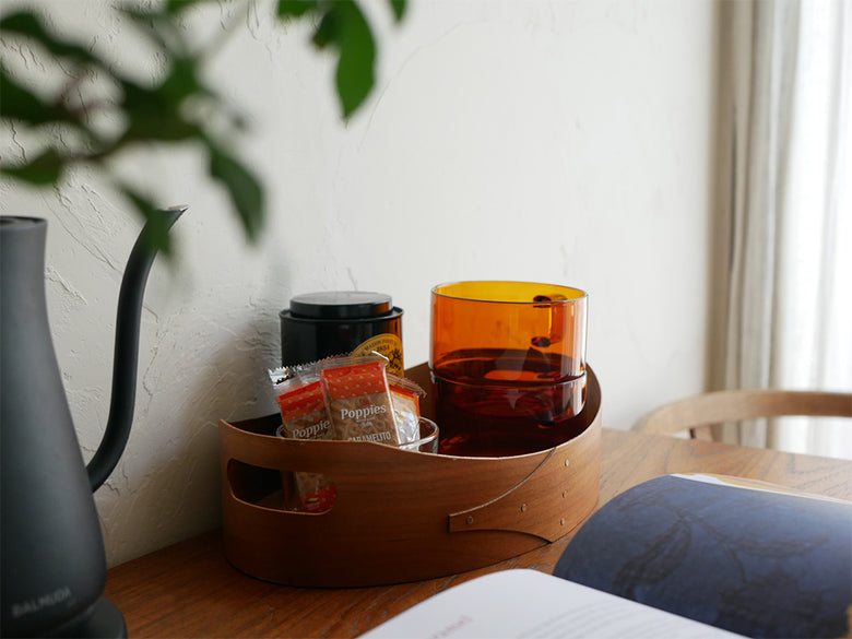 ハリオの耐熱ガラス製コールドブリューピッチャーとスタックマグカップが木目調のテーブルに配置された静物写真