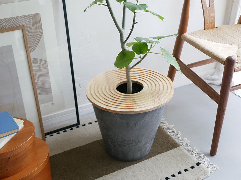 天然木製のプラントテーブルに鉢植えが置かれ、土が隠れるナチュラルなデザイン