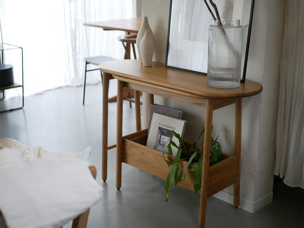オーク無垢材で作られた伸長可能なコンソールテーブル「SUK」が木製の床の上に配置され、観葉植物が添えられたインテリアシーン