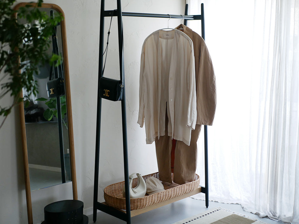 ラタンバスケット付きオーク無垢材フレームのホワイトコートハンガーに衣類が掛けられている様子