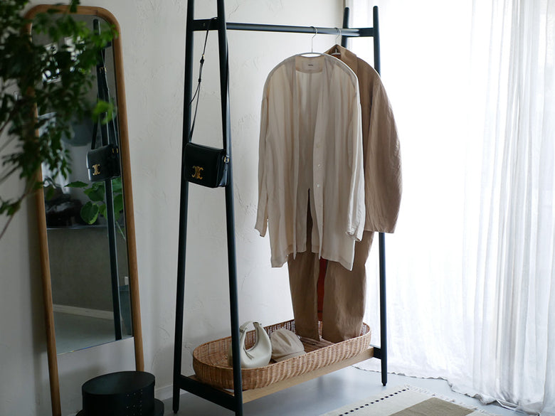 ラタンバスケット付きオーク無垢材フレームのホワイトコートハンガーに衣類が掛けられている様子