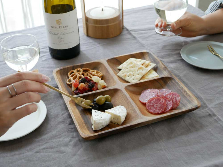 天然アカシア木製のエッグ型トレー、スクエアトレー、ラウンドボールが木のテーブル上に並べられ、チーズやプレートなどの料理が盛り付けられている