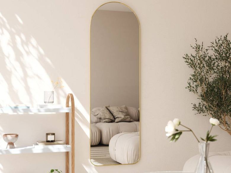リビングルームに置かれたウムブラ フーバ アーチド リー二ングミラー。天然素材のフレームとガラス部分が特徴で、隣にランプや観葉植物が配置されています。