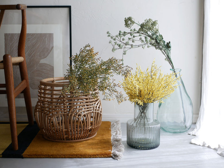 籐製の収納バスケットにアデペシュのアーティフィシャルフラワーが美しくアレンジされた室内ディスプレイ