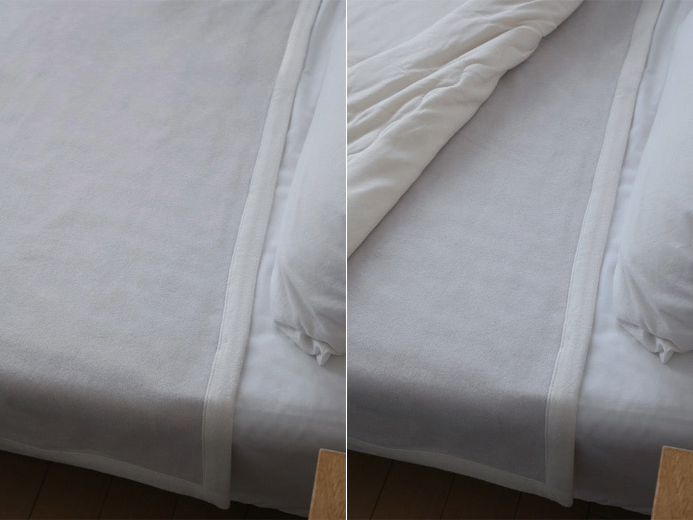 白いオーガニックコットン毛布が敷かれたシングルサイズのベッドと、シルバーの寝具が備えられた明るい寝室の写真