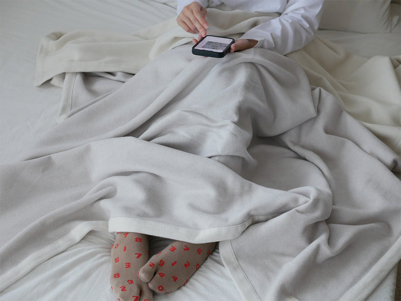 シングルサイズのcocomaniオーガニックコットン毛布がベッドに優しくかけられている様子