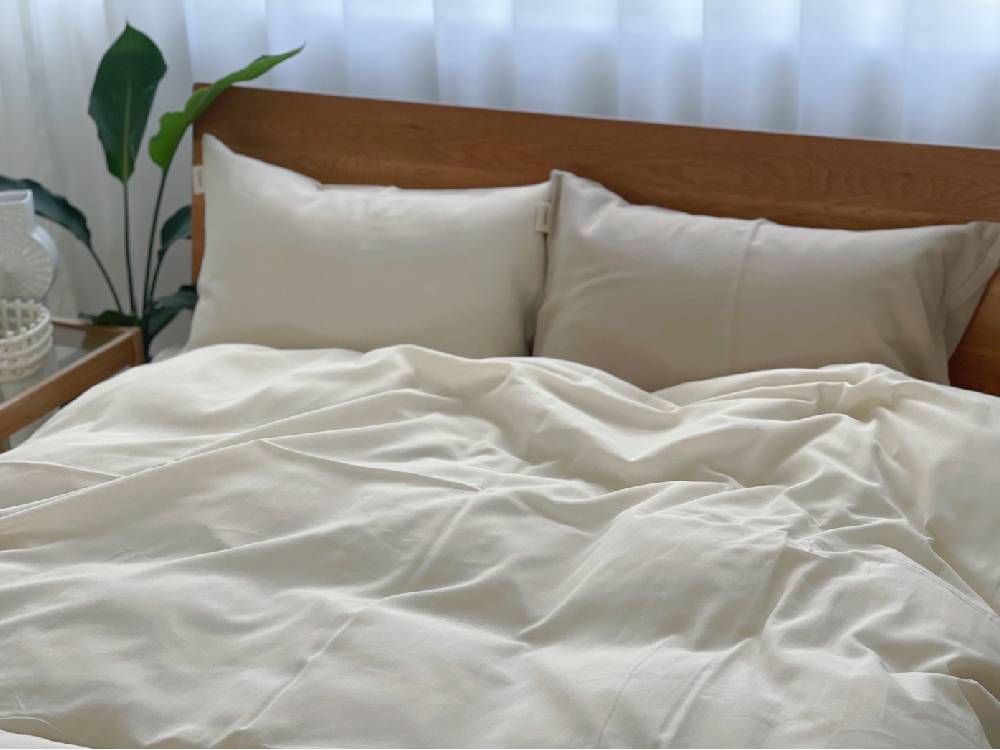 オーガニックコットン100%のシングルサイズ布団カバーが整えられたベッドと、枕やクッションが配置された快適な寝室の様子