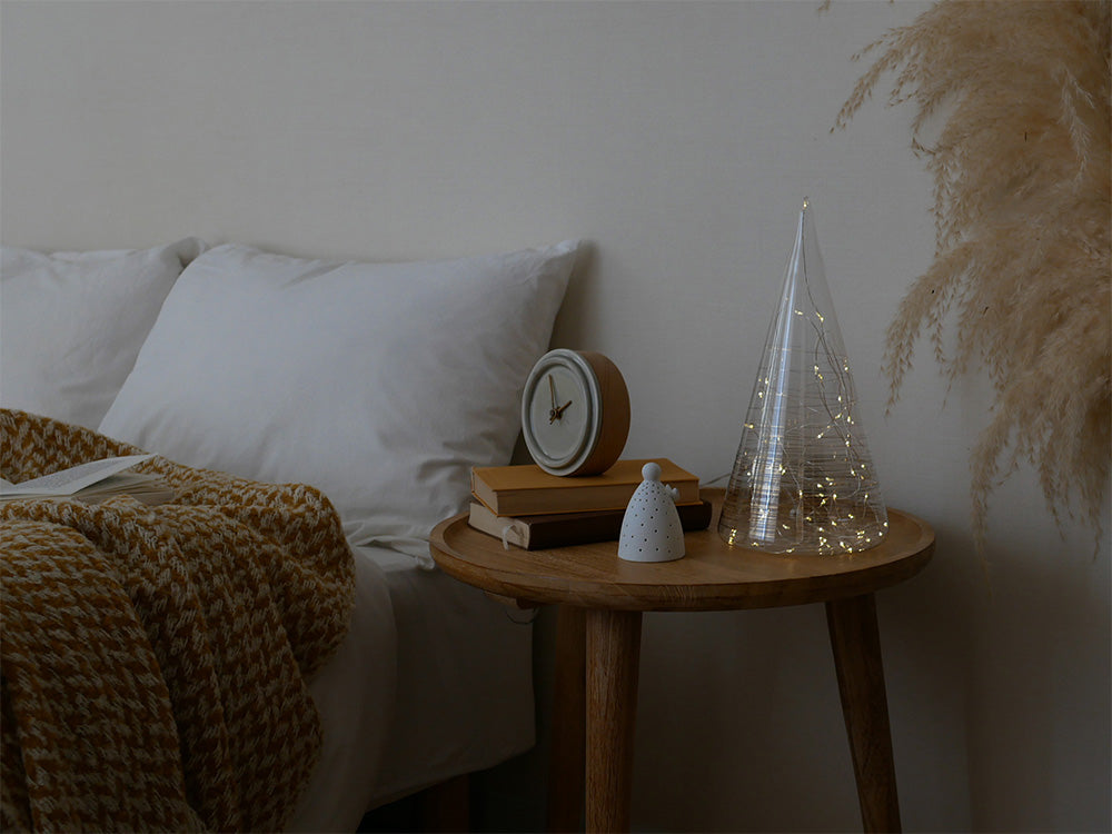 ベッドルームに配置されたハードウッドのランプと自然素材の家具、観葉植物、寝具が調和したインテリア