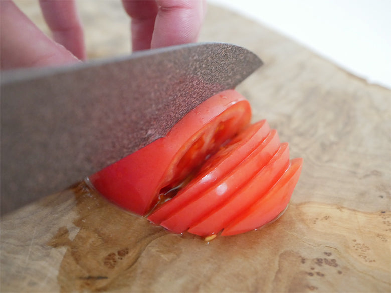 カッティングボード上に協和工業のストーンバリア包丁とシャープナーが置かれ、プラムトマトや野菜が並んでいる様子