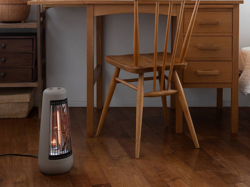 プラスマイナスゼロ カーボンヒーター H210が木製のフローリングとランプと共に配置された室内の様子