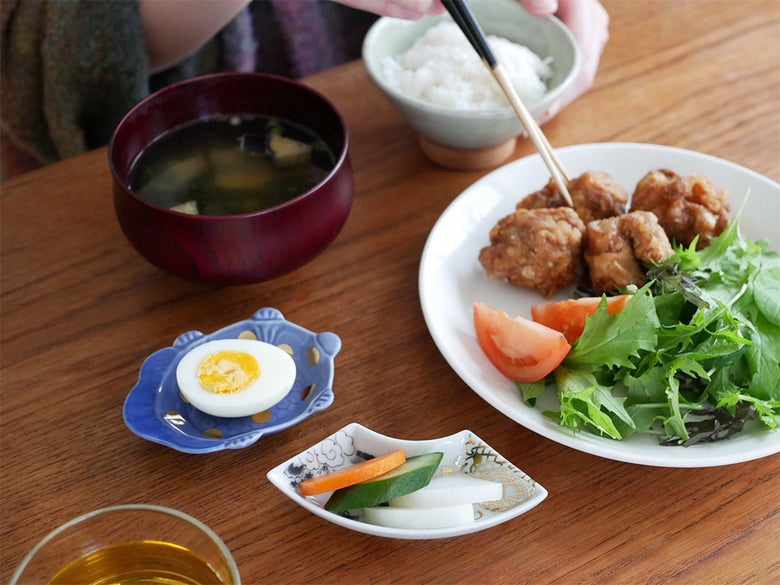 アマブロのMAMEシリーズに属する多種類の磁器製テーブルウェアが、食事と共にテーブルに美しく配置されている写真