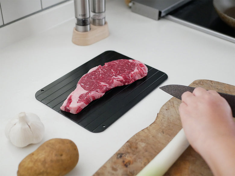 CBJAPANのアルミ製解凍プレート上に、まな板と牛肉や豚肉などの食材が並べられている調理中のキッチンシーン