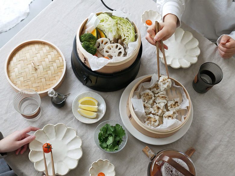 ほったらかし電気せいろと盛り付けられた料理と食器が並ぶ食卓の写真