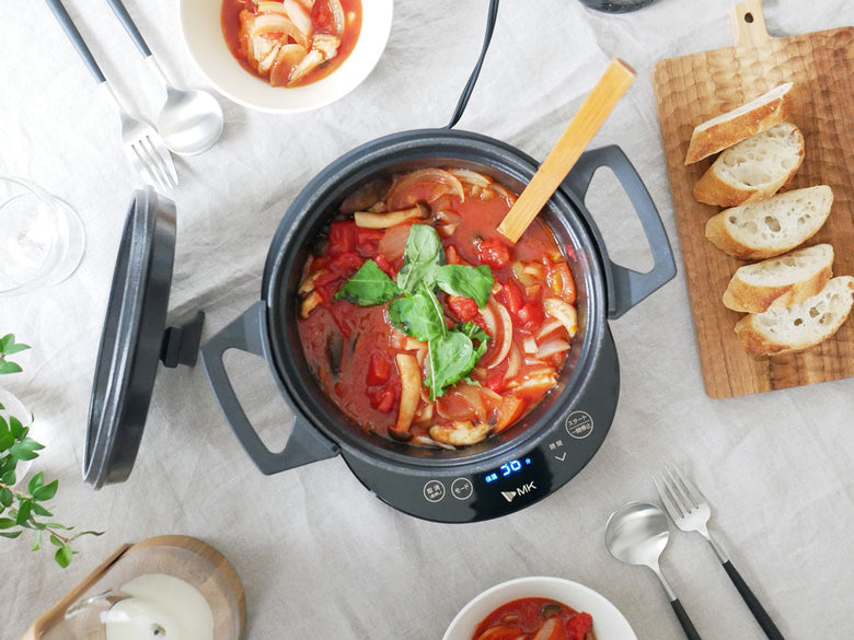 水無し電気鍋 KO TSU I RA ZUと鍋セット、調理中の野菜、テーブルウェアがキッチンテーブルに配置されている様子