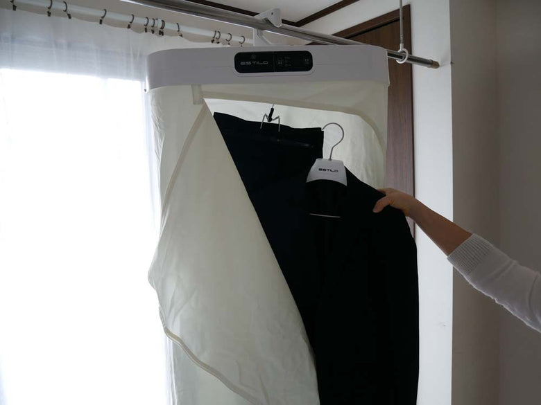 ESTILOエスティロのスチームイオンリフレッシャーがクローゼット内でハンガーやカーテンと共に展示されている様子