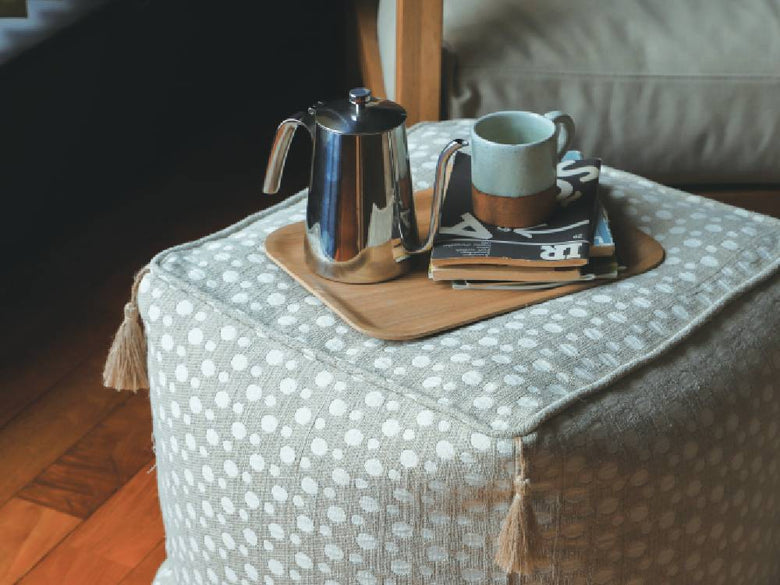 グレーのアデペシュ製フレンチリネンビーズクッションがリビングルームのオットマンと共に配置されている