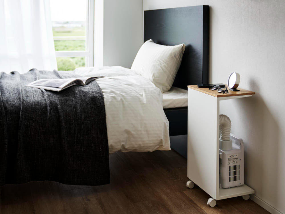 タワーキャスター付き目隠し布団乾燥機スタンドが木製フロアのベッドルームに配置されている様子