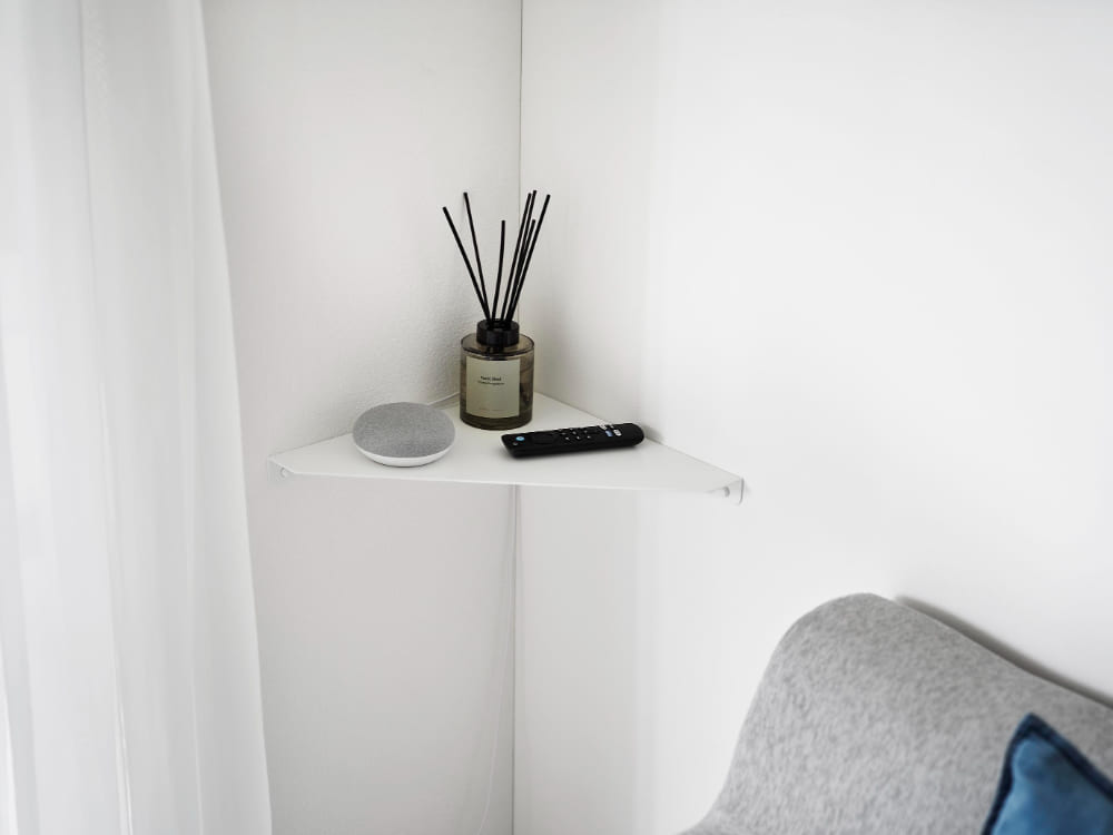 リビングルームの壁に設置された『tower』石こうボード対応のウォールコーナーシェルフ。スチール製の棚にランプやクッションが飾られています。