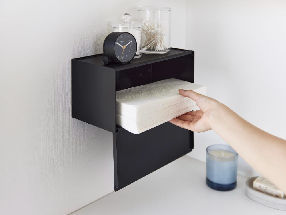 石こうボード対応トレー付きペーパータオルディスペンサーが棚に設置され、書類やオフィス用品、観葉植物、花瓶などが周囲に配置されています