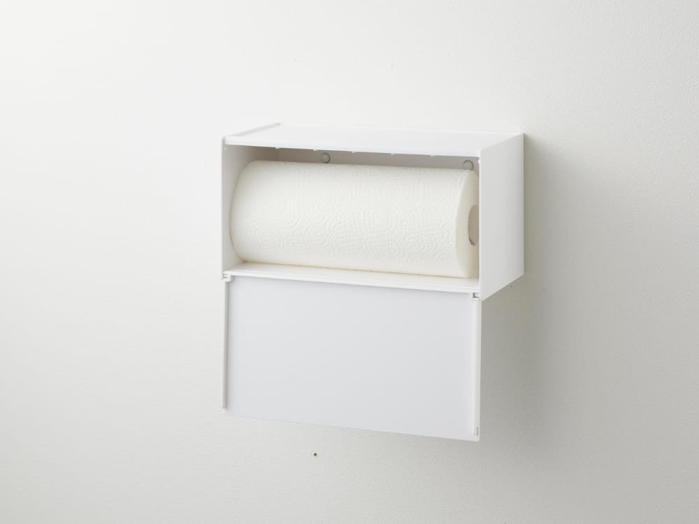 石こうボード対応のトレー付きペーパータオルディスペンサー。白色のシリンダー型本体が壁に取り付けられており、下部にペーパートレーが付属しています。