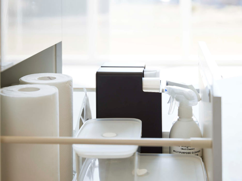 タワーのスリムプラスチックバッグケースが棚に置かれ、トイレットペーパーやキッチンペーパーなどの家庭用紙製品を整理している様子