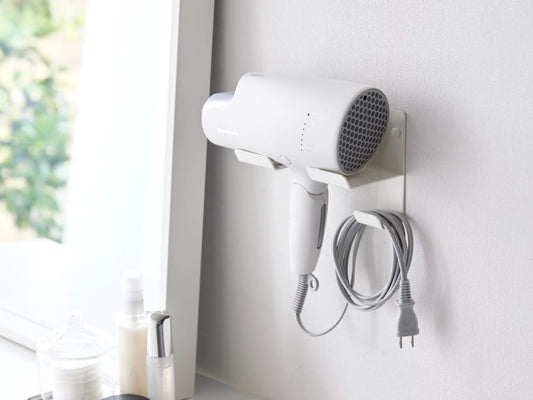 壁に取り付けられたスチール製のウォールドライヤーホルダーにヘアドライヤーが掛かっている様子